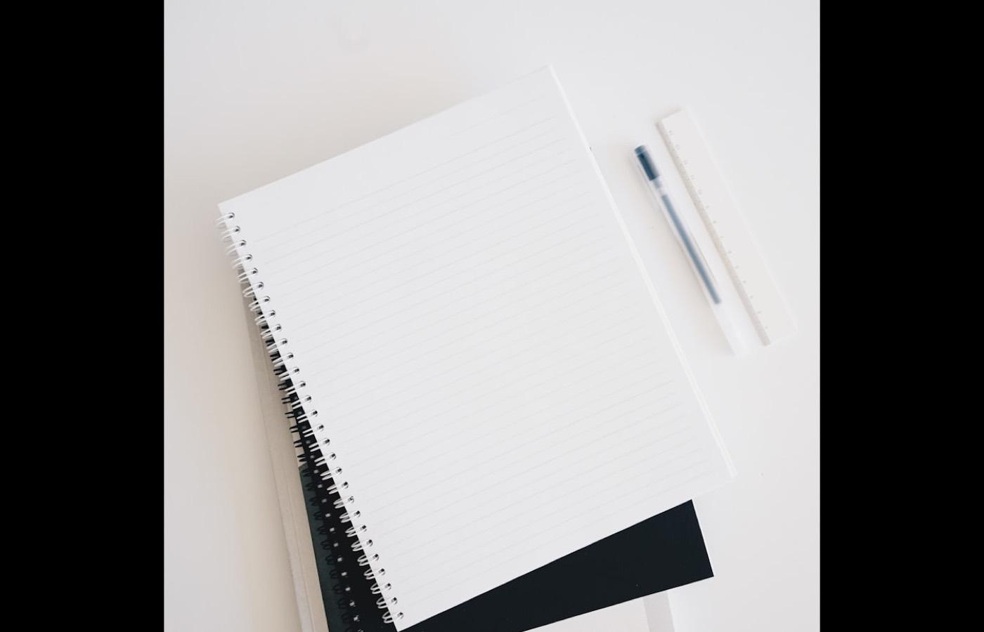 A blank spiral notebook and a pen on a pale desk.