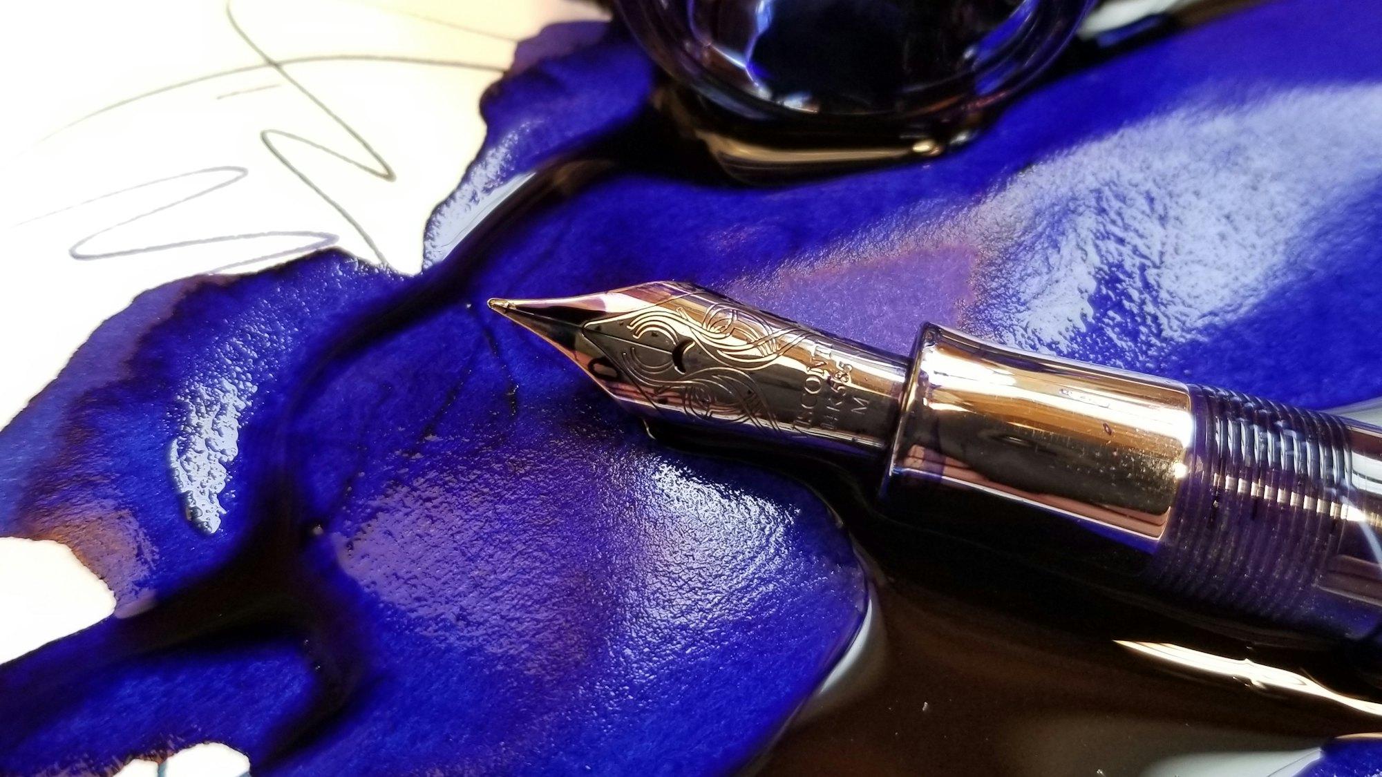 A fountain pen nib resting in a pool of wet blue ink.