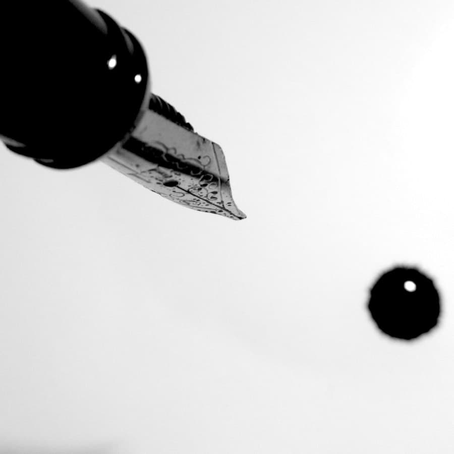 A fountain pen nib with a drop of ink falling from it.